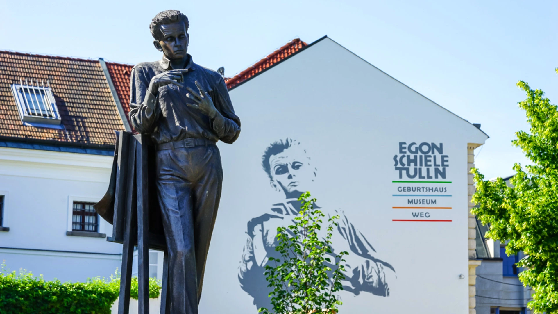 Statue des Künstlers Egon Schiele vor einem Gebäude mit großflächigem Wandbild und Schriftzug Egon Schiele Tulln.