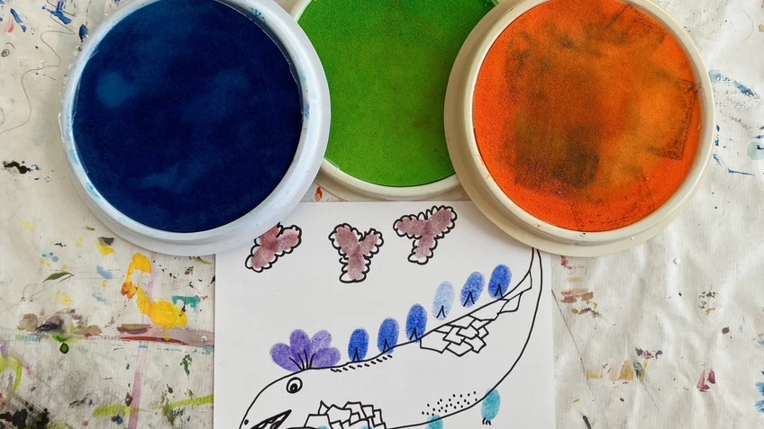Fingerfarben in blau, grün und orange und eine Zeichnung eines Tiers, das mit Fingerfarben gemalt wurde