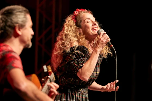 Frau mit langen blonden Locken singt strahlend in ein Mikrophon