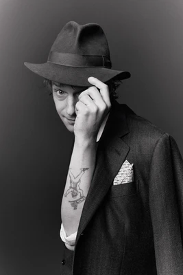 Porträtfoto des Musikers Voodoo Jürgens in schwarz-weiß, der mit auffälligem Hut Richtung Kamera grüßt.