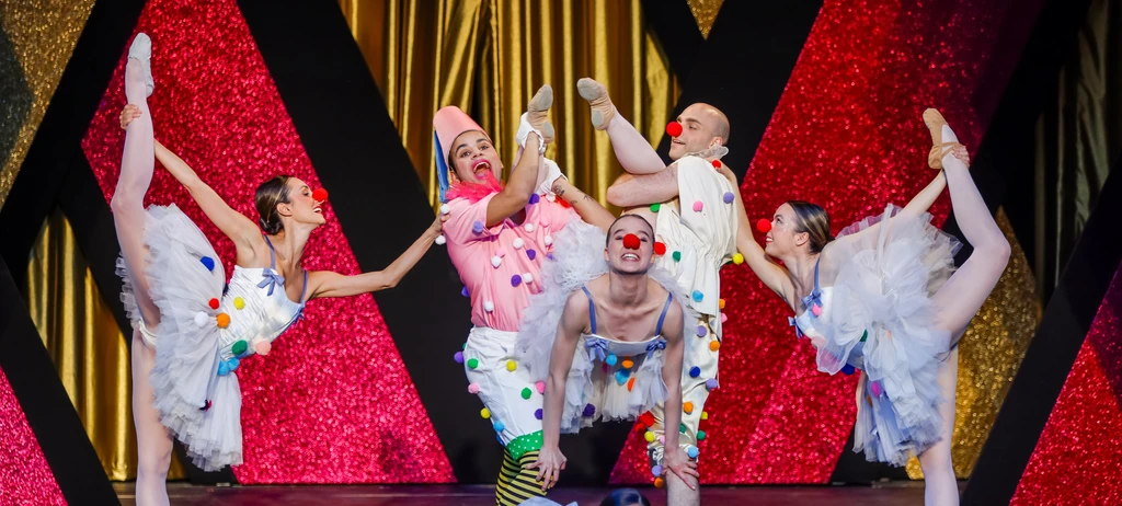 Drei Frauen und zwei Männer mit roten Clownnasen und in Clownkostümen bewegen sich in Ballettposen vor rot-goldenem Hintergrund.