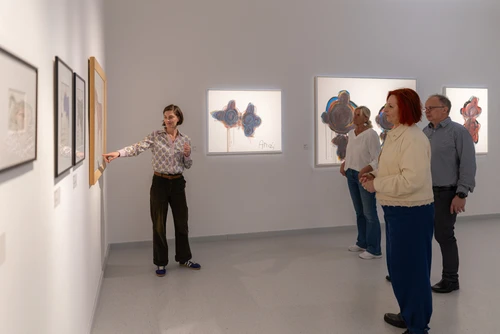 Eine Person zeigt im Museum auf ein Bild hin, während drei weitere Personen zuhörend sich das Bild ansehen.