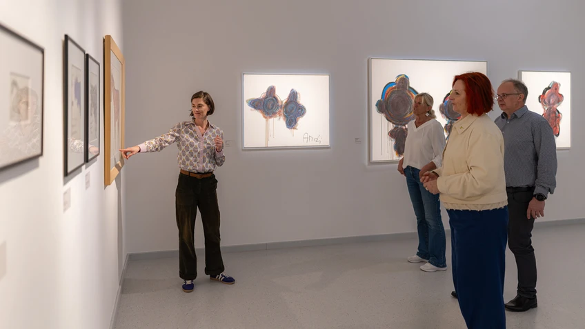 Eine Person zeigt im Museum auf ein Bild hin, während drei weitere Personen zuhörend sich das Bild ansehen.