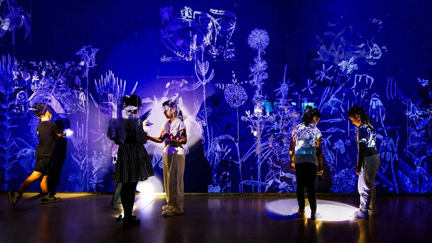 Fünf Kinder leuchten mit Taschenlampen in einem dunklen Raum. Hinter ihnen befindet sich eine dunkelblaue Wand, mit weißen Naturprojektionen. Vor ihnen hängen Plexiglaselemente mit eingeritzten Zeichnungen von Robert Gabris, Iva Ivanova und Theodor Moise.
